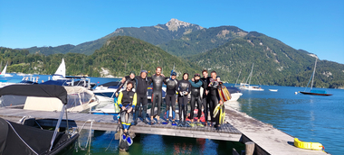 Die Gruppe der Schwimmlehrer:innenausbildung 2023 am Steg, am Wolfgangsee. Alle tragen Taucheranzüge