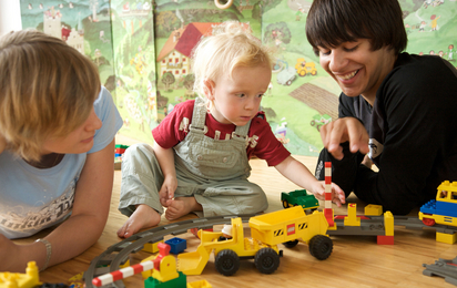 Babyfit 2009. Ausbildung (Kurs) zum Babysitter. Jugendliche/Teenager. Junge und Mädchen spielen mit Kleinkind am Boden mit Legosteinen und Spielzeugeisenbahn. Querformat.