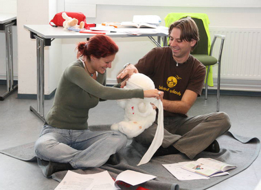 Ein Mann und eine Frau sitzen auf dem Boden und verarzten einen Rotkreuz-Teddybären im Zuge der Erste-Hilfe-Lehrbeauftragten-Ausbildung des Österreichische Jugendrotkreuzes.