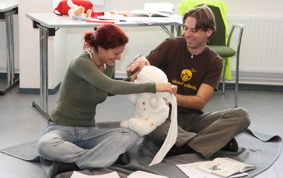 Ein Mann und eine Frau sitzen auf dem Boden und verarzten einen Rotkreuz-Teddybären im Zuge der Erste-Hilfe-Lehrbeauftragten-Ausbildung des Österreichische Jugendrotkreuzes.