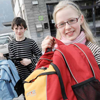 Mädchen und Bub präsentieren ihre gesammelten Schultaschen vor der Schule