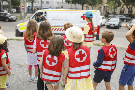 Kinder in roten Warnwesten schauen sich ein Rettungsauto an.