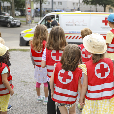 Kinder in roten Warnwesten schauen sich ein Rettungsauto an.