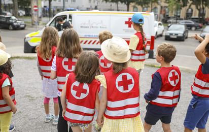 Kinder in roten Warnwesten schauen sich ein Rettungsauto an.