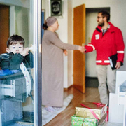 Ein Jugendrotkreuz-Mitarbeiter übergibt Weihnachtspakete eine eine alleinerziehende Mutter und ihren Sohn.