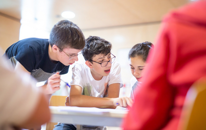 3 Jugendliche bzw. Kinder lesen in einer angelehnten Pose einen Zettel.