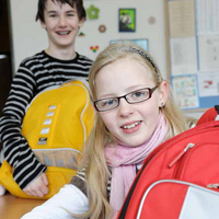 Mädchen und Bub präsentieren ihre gesammelten Schultaschen in der Klasse