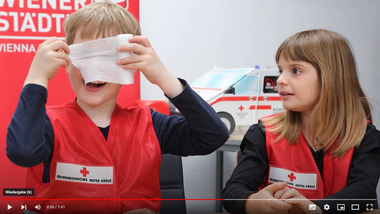 Zwei Kindergartenkinder, der Bub hält sich einen Verband vors Gesicht, das Mädchen beobachtet ihn