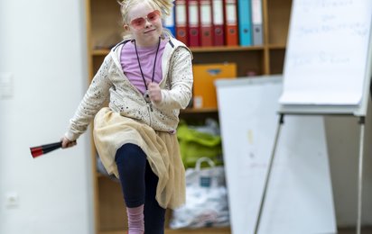 Ein Mädchen tanzt mit pinker Sonnenbrille und hellgelbem Rock vergnügt durch den Raum.