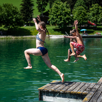 Kinder springen mit Anlauf von einem Steg in einen Badesee.