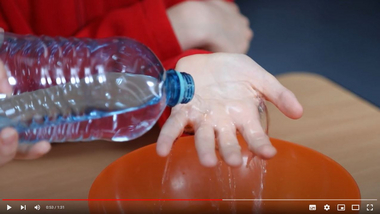 Ein Kind zeigt wie man bei einer Verbrennung Wasser aus einer Flasche über die Hand laufen lässt