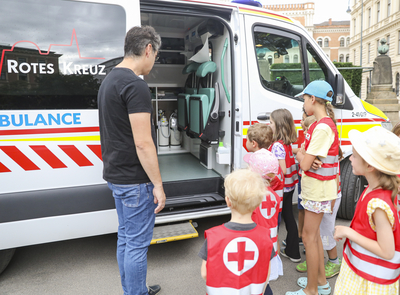 Kinder in roten Warnwesten bekommen ein Rettungsauto erklärt