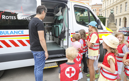 Kinder in roten Warnwesten bekommen ein Rettungsauto erklärt