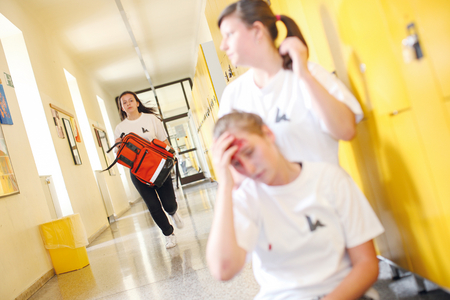 Eine Schüler*in ist verletzt und zwei andere Kinder leisten Erste Hilfe.