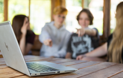 Vier Jugendliche sitzen am Tisch und zeigen in Richtung Laptop.