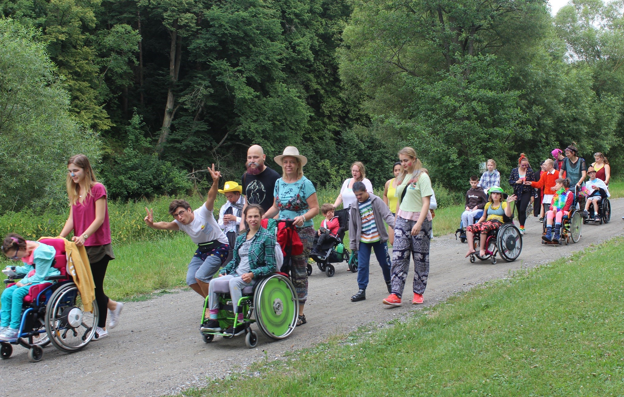 Eine Gruppe von Kinder und Jugendlichen mit Behinderungen und ihre Betreuer:inen spazieren gemeinsam auf einem Waldweg.