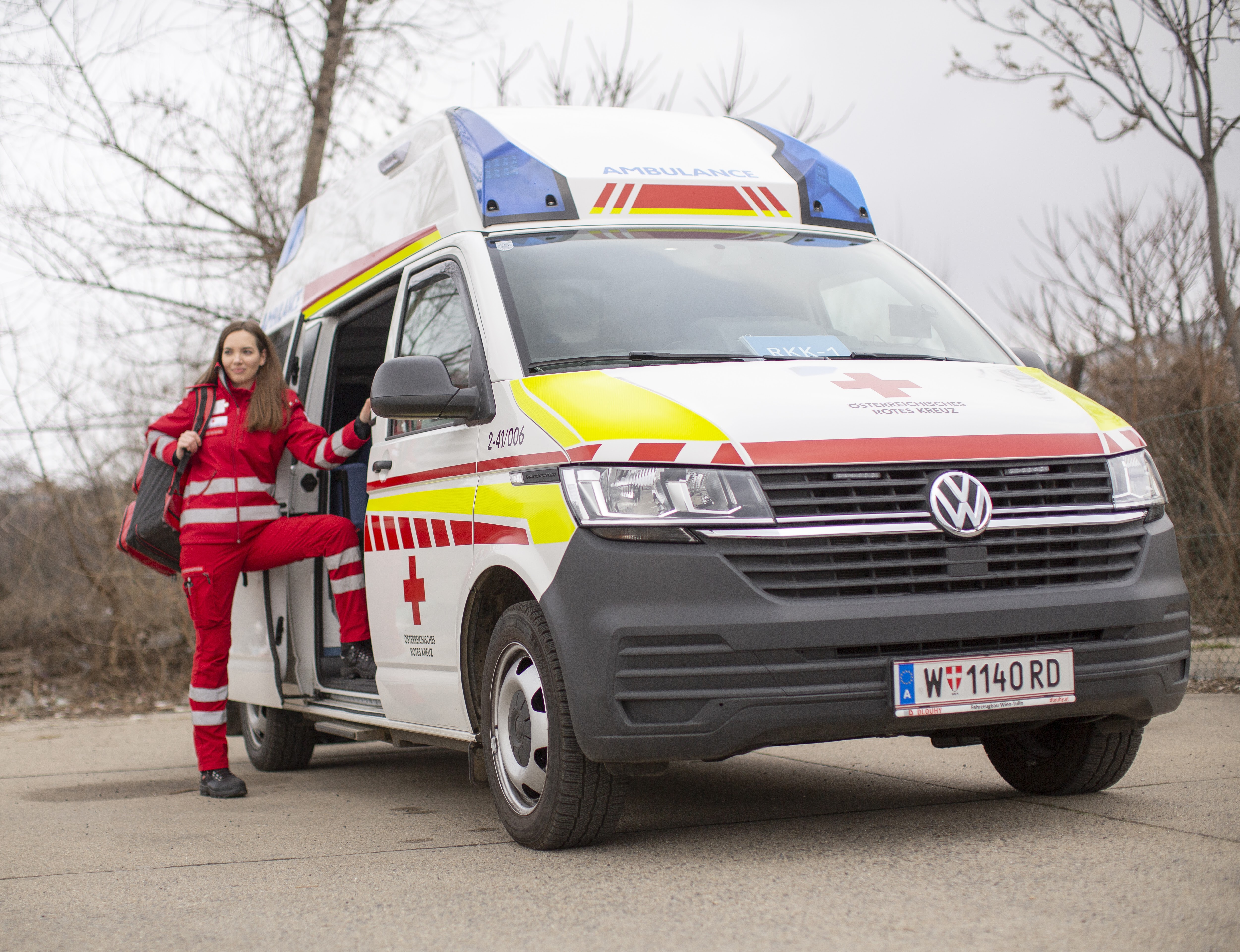 Eine junge weibliche Sanitäterin steht bei einem Rettungsauto des Roten Kreuzes